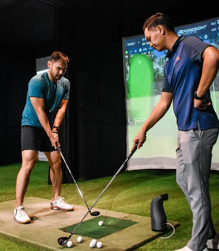 A GolfX coach with a golfer in a simulator bay